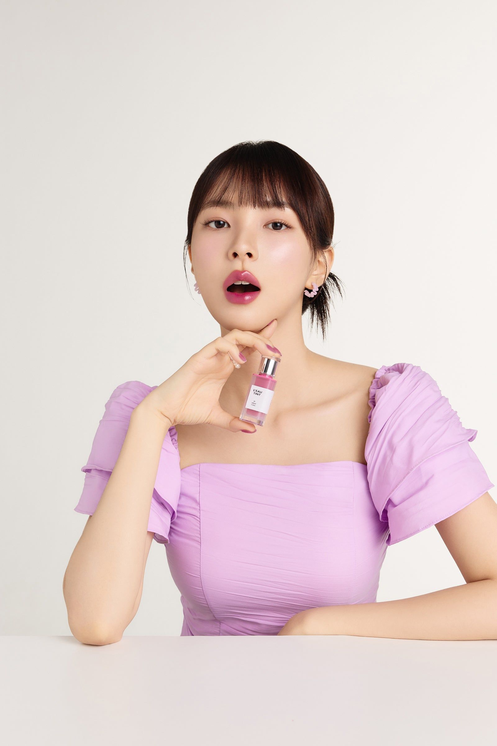 Frau hält BBIA L'eau Tint 03 Lilac L'eau. Sie trägt ein lilafarbenes Oberteil.