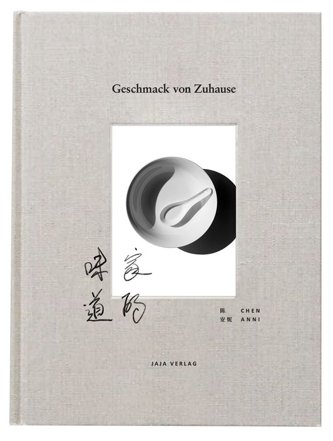 Buch mit Leinen-Einband. Titel: Geschmack von Zuhause. Inset: Schale mit Löffel. Schriftzeichen und Autorenname. Verlag: JAJA VERLAG.