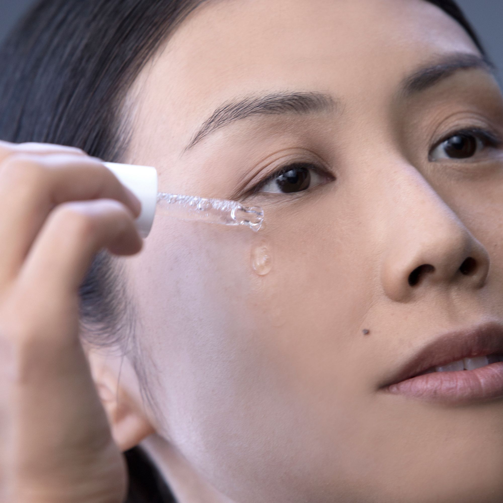 Eine Frau trägt Alkemy Pure Collagen Serum mit einer Pipette auf ihr Auge auf.