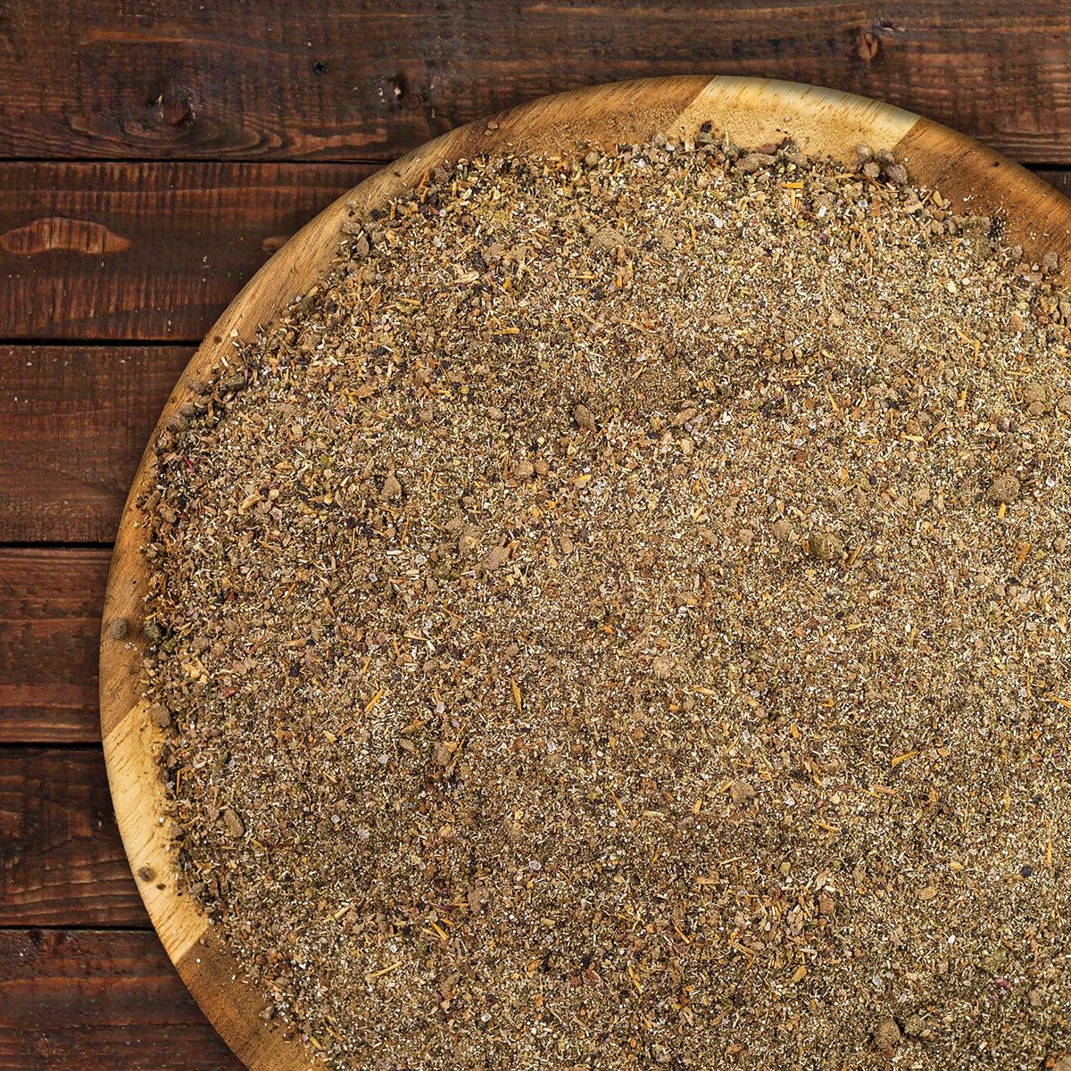 Runder, hölzerner Teller mit braunem, körnigem Futter. Auf Holzuntergrund platziert.