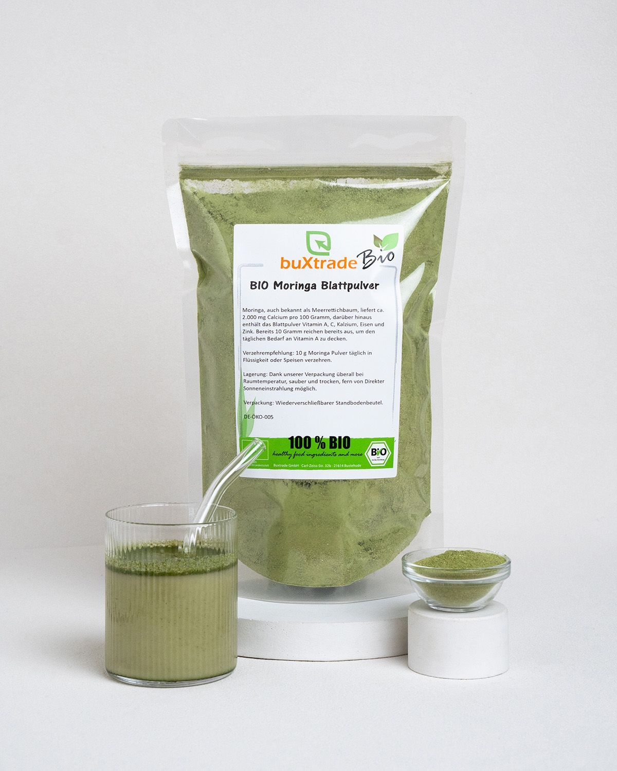 Beutel, Glas mit Getränk, Schale mit Pulver. Etikett: buXtrade Bio Moringa Blattpulver.