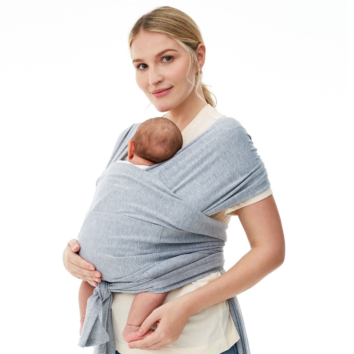 Een lichtgrijze Momcozy draagdoek gedragen door een vrouw die een baby vasthoudt. De doek is om het lichaam van de vrouw gewikkeld en de baby wordt er veilig in gehouden. Het Momcozy-logo is zichtbaar op de doek.