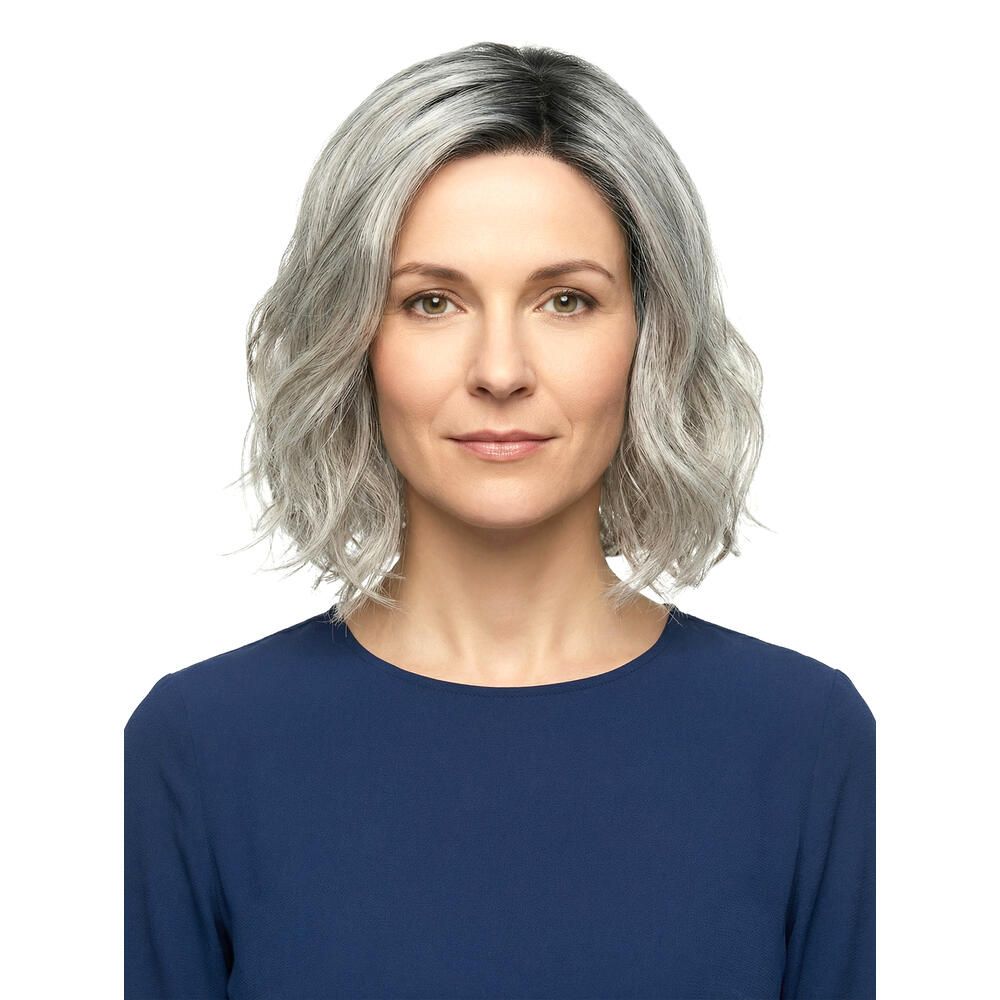 Grau-meliertes Haar, schulterlang, gewellt. Die Frau trägt ein blaues Oberteil. Frontalansicht.
