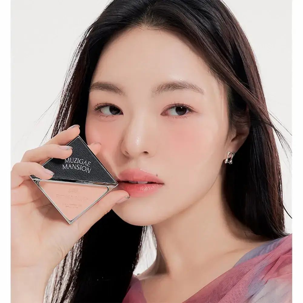 Rouge in schwarzer, quadratischer Verpackung, gehalten von einer Person. Auf der Verpackung steht MUZIGAE MANSION.