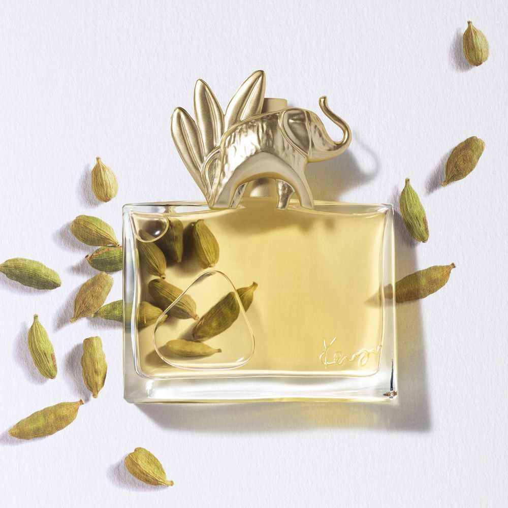 Parfümflakon mit goldenem Elefanten-Deckel, umgeben von grünen Kapseln. Klarer Glasbehälter mit gelblicher Flüssigkeit.