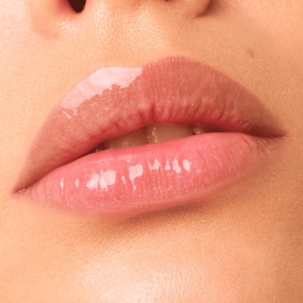 Nahaufnahme von Lippen mit aufgetragenem Lipgloss. Glänzendes Finish. Rosa Farbton. Haut um die Lippen sichtbar.