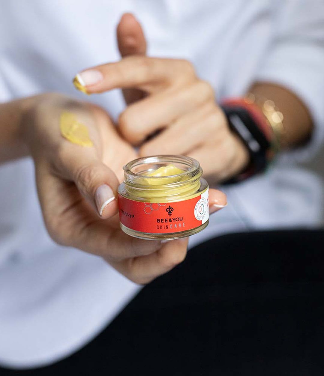 Person hält Creme-Tiegel und Creme auf der Hand. Aufschrift: BEE&YOU Skincare. Creme gelb.