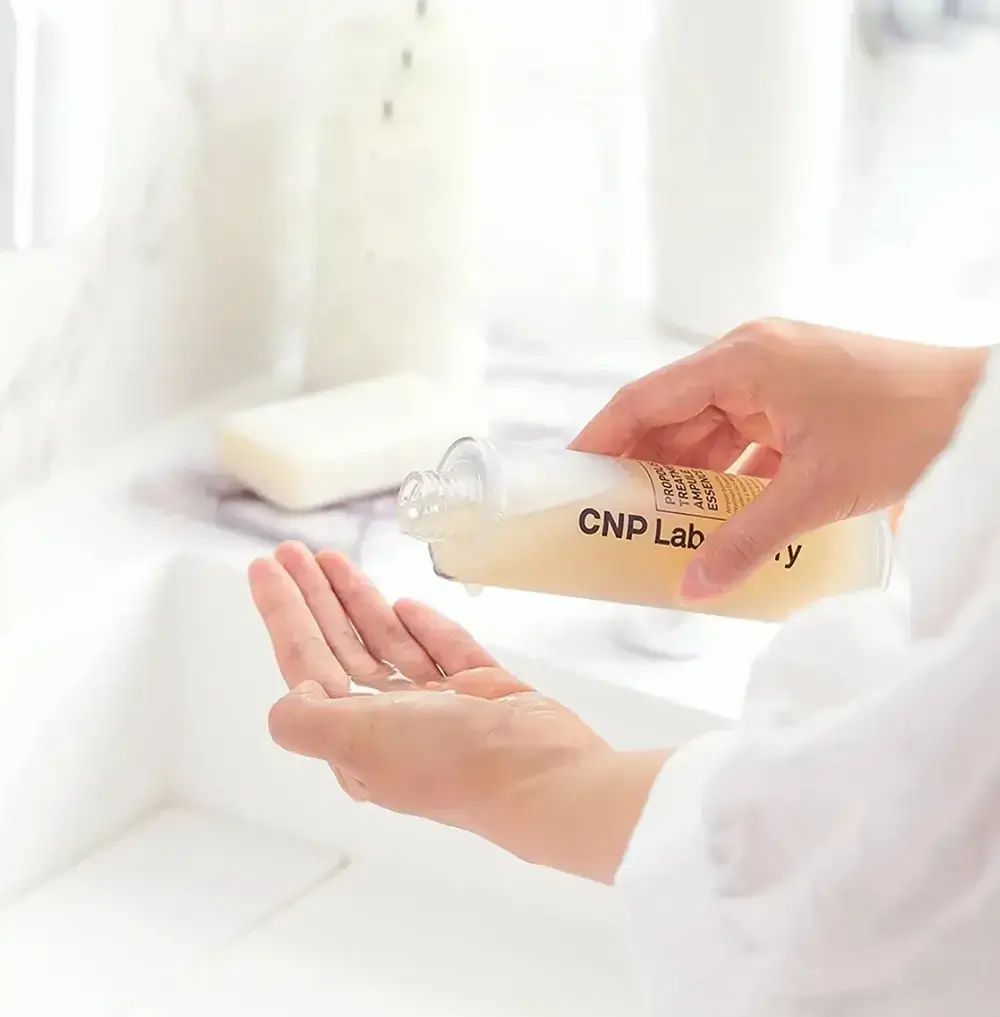 Person gießt CNP Laboratory Propolis Treatment Ampoule in die Hand. Flasche mit Produktetikett. Badezimmerhintergrund.
