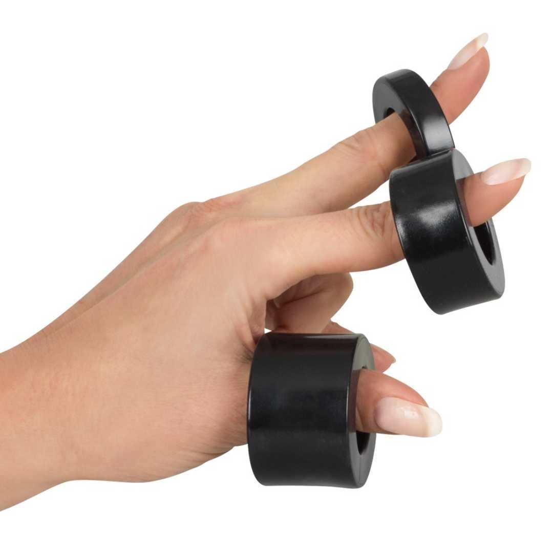 Hand mit drei schwarzen Ringen auf den Fingern. Ringe zylindrisch, mit Loch.