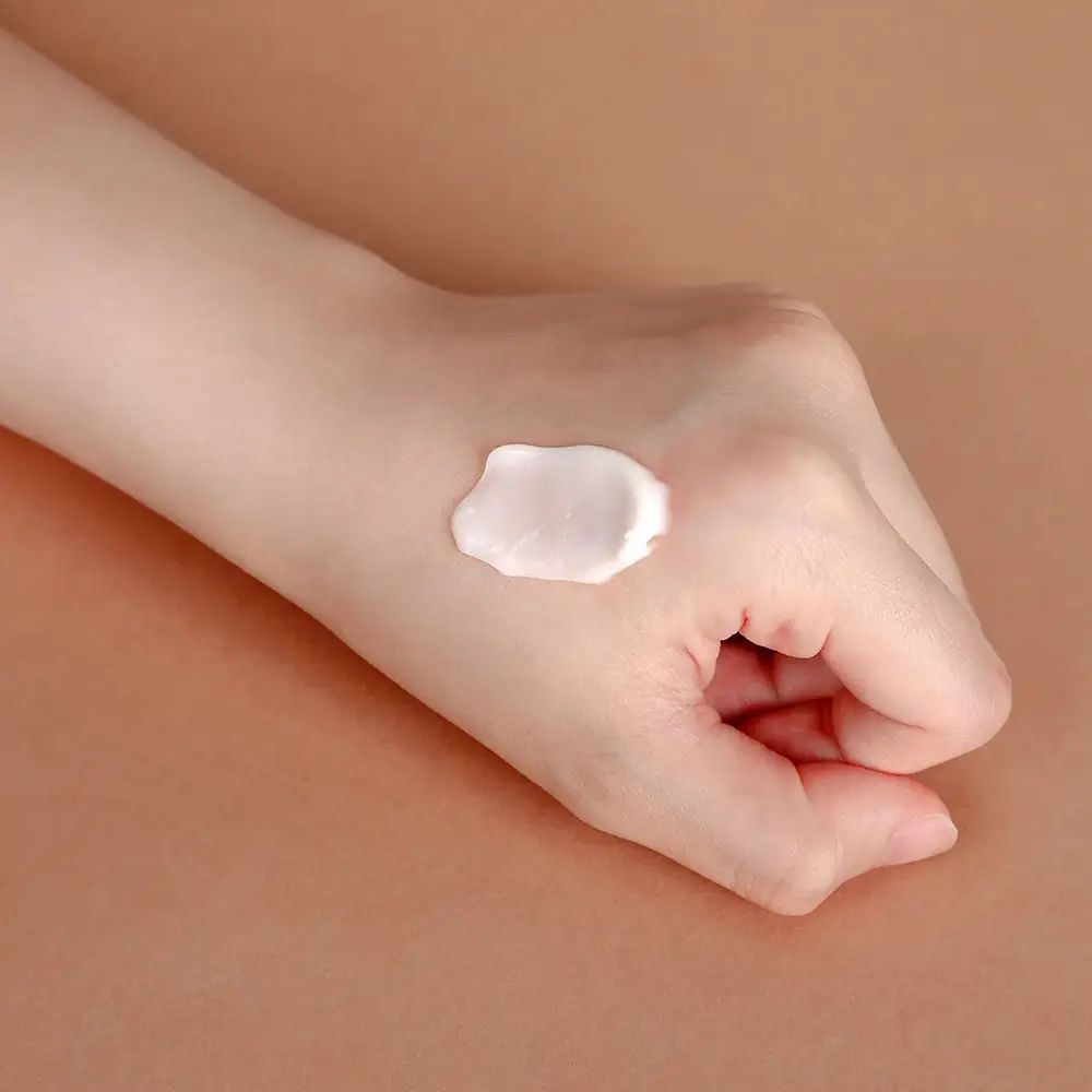 Hand mit Creme auf braunem Hintergrund. Creme-Klecks auf der Handfläche.