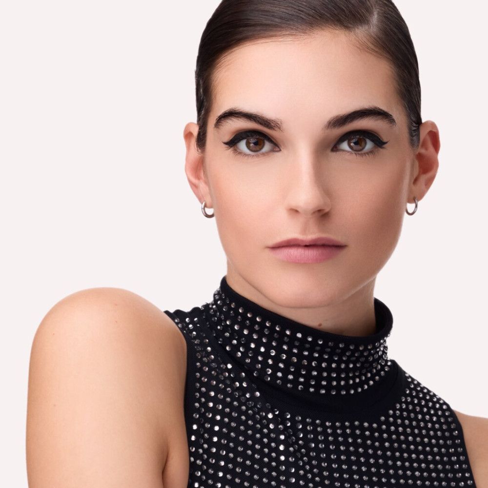 Porträt einer Frau mit schwarzem Eyeliner. Sie trägt ein schwarzes Oberteil mit silbernen Verzierungen.