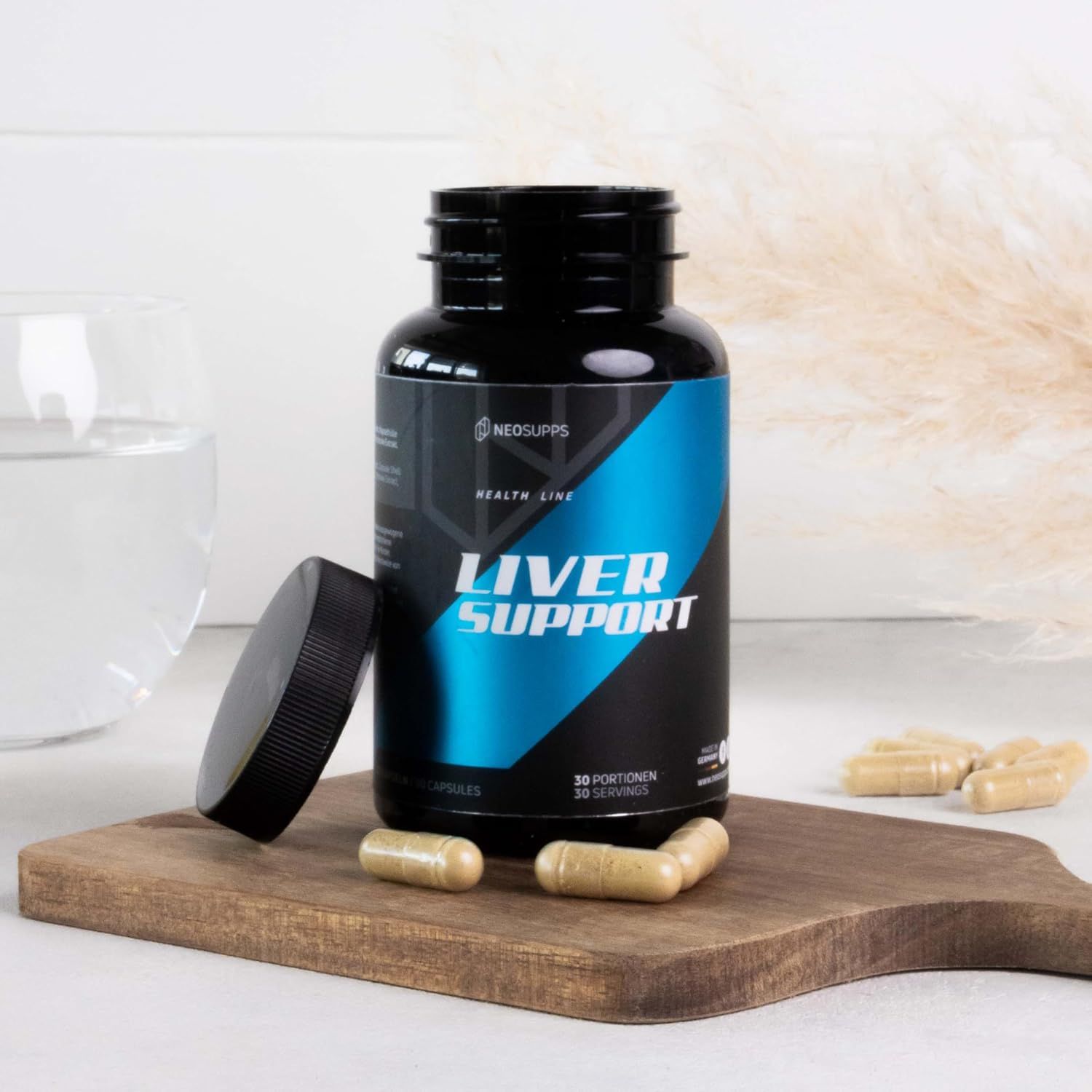 Schwarze Flasche "LIVER SUPPORT" mit geöffnetem Deckel und Kapseln auf einem Holzbrett. Einige Kapseln liegen verstreut.