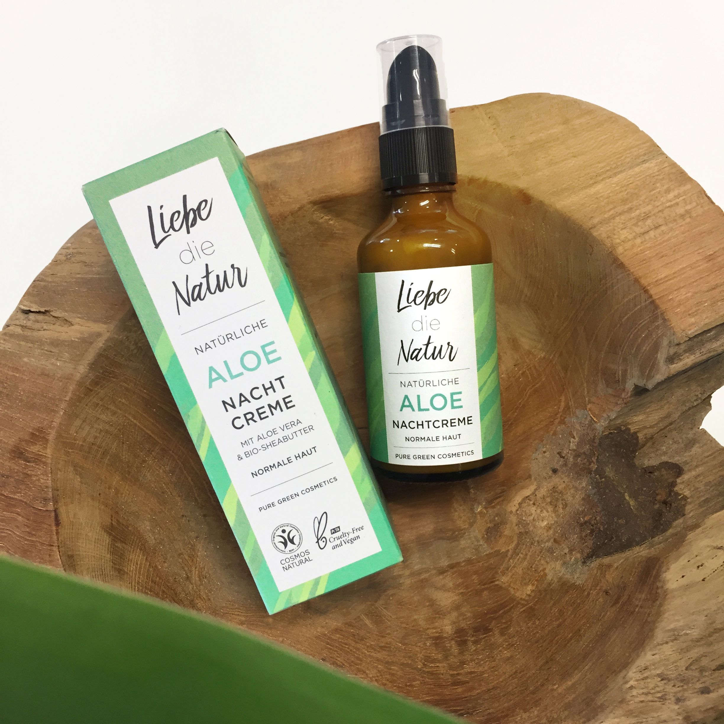Braune Glasflasche und Schachtel mit Aufschrift 'Liebe die Natur Aloe Nachtcreme'. Grüne Etiketten, Holzuntergrund.