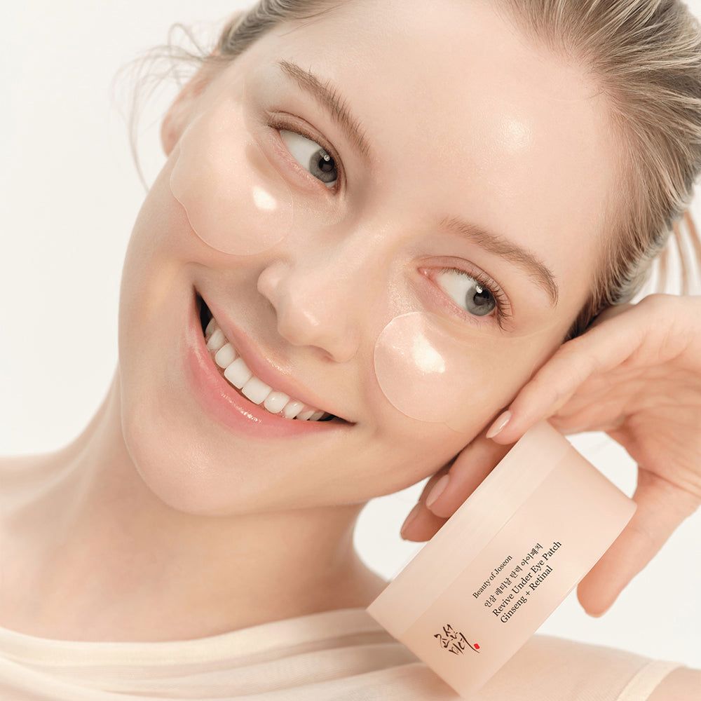 Frau mit Augenpads und Produktbox. Die Box zeigt 'Revive Under Eye Patch Ginseng + Retinol'.