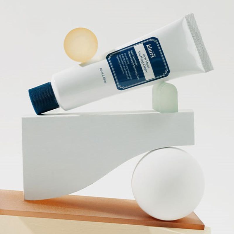 Weiße Tube mit blauem Verschluss auf geometrischen Formen. Aufschrift: Klairs Rich Moist Soothing Cream.