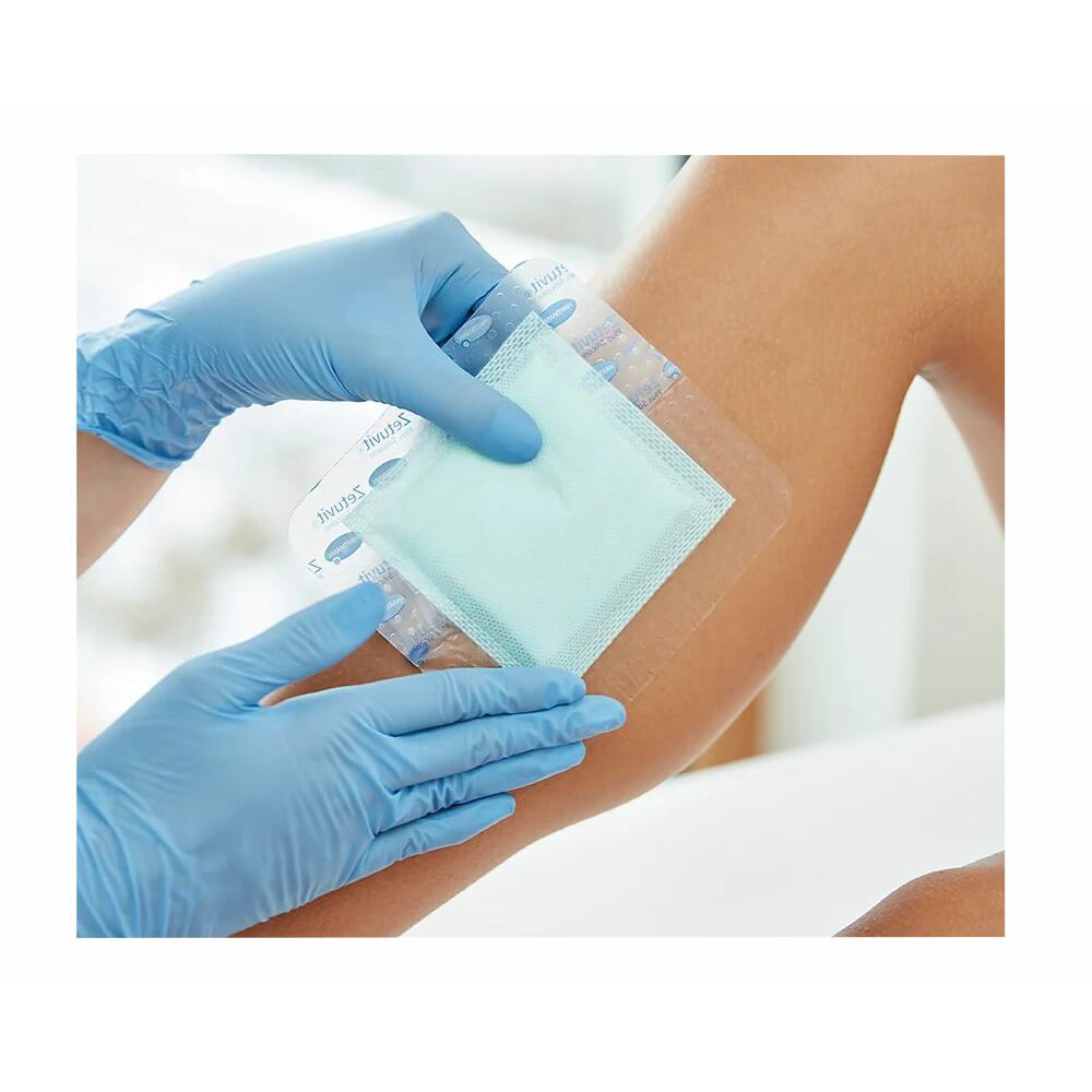 Persona tiene Zetuvit Plus Silicone Border. Compressa quadrata con tampone blu. Confezionato in pellicola. Applicazione sul braccio.