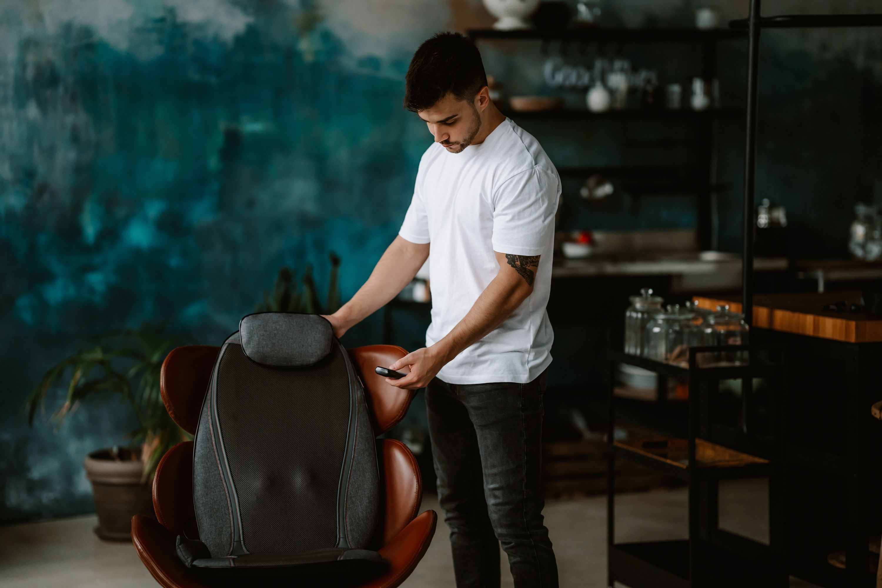 Mann mit weißem T-Shirt und Jeans steht neben einer Shiatsu-Massagematte. Er hält ein Bedienfeld in der Hand.