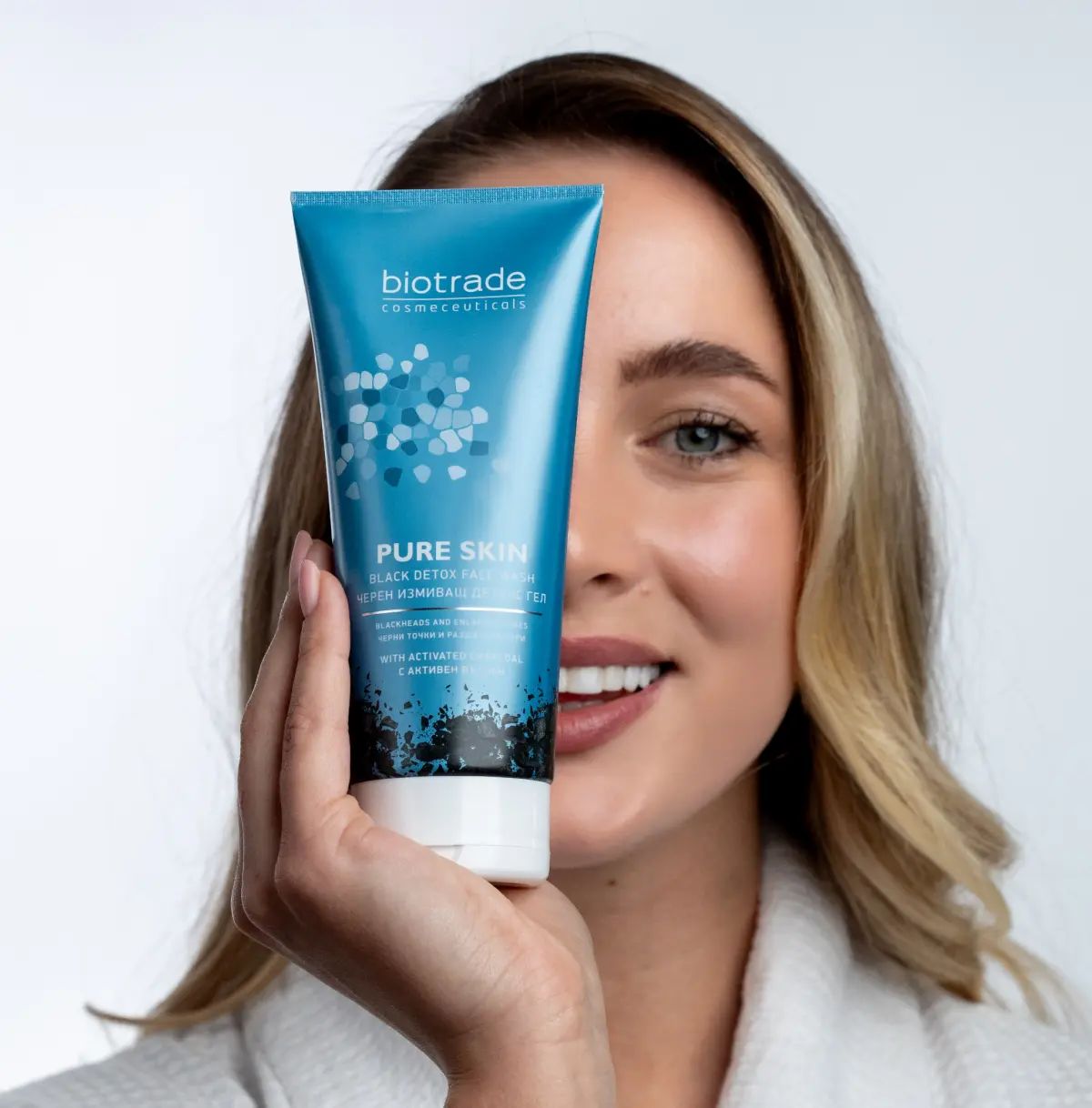 Frau hält eine blau-graue Tube vor ihr Gesicht. Aufschrift: Biotrade, Pure Skin Black Detox Face Wash.