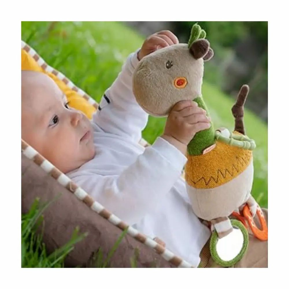 Baby hält Kuscheltier-Giraffe. Beige, grün und gelb. Mit Ringen und Spiegeln. Aufschrift "Lotta". Baby liegt in einer Wippe.