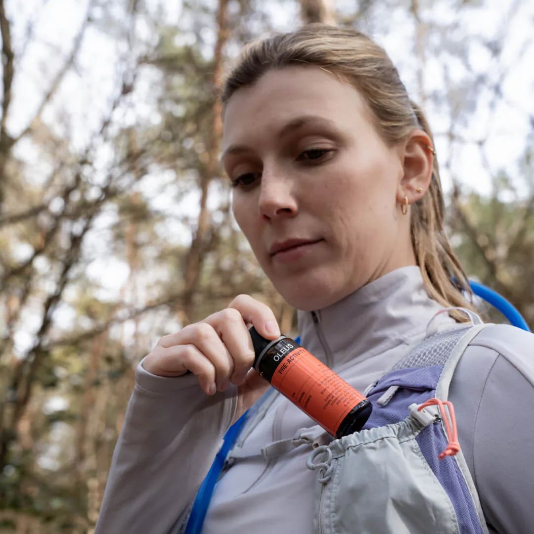 Frau mit Flasche in Rucksacktasche. Flasche mit Etikett. OLEUS-Logo und Produktinformationen sichtbar.