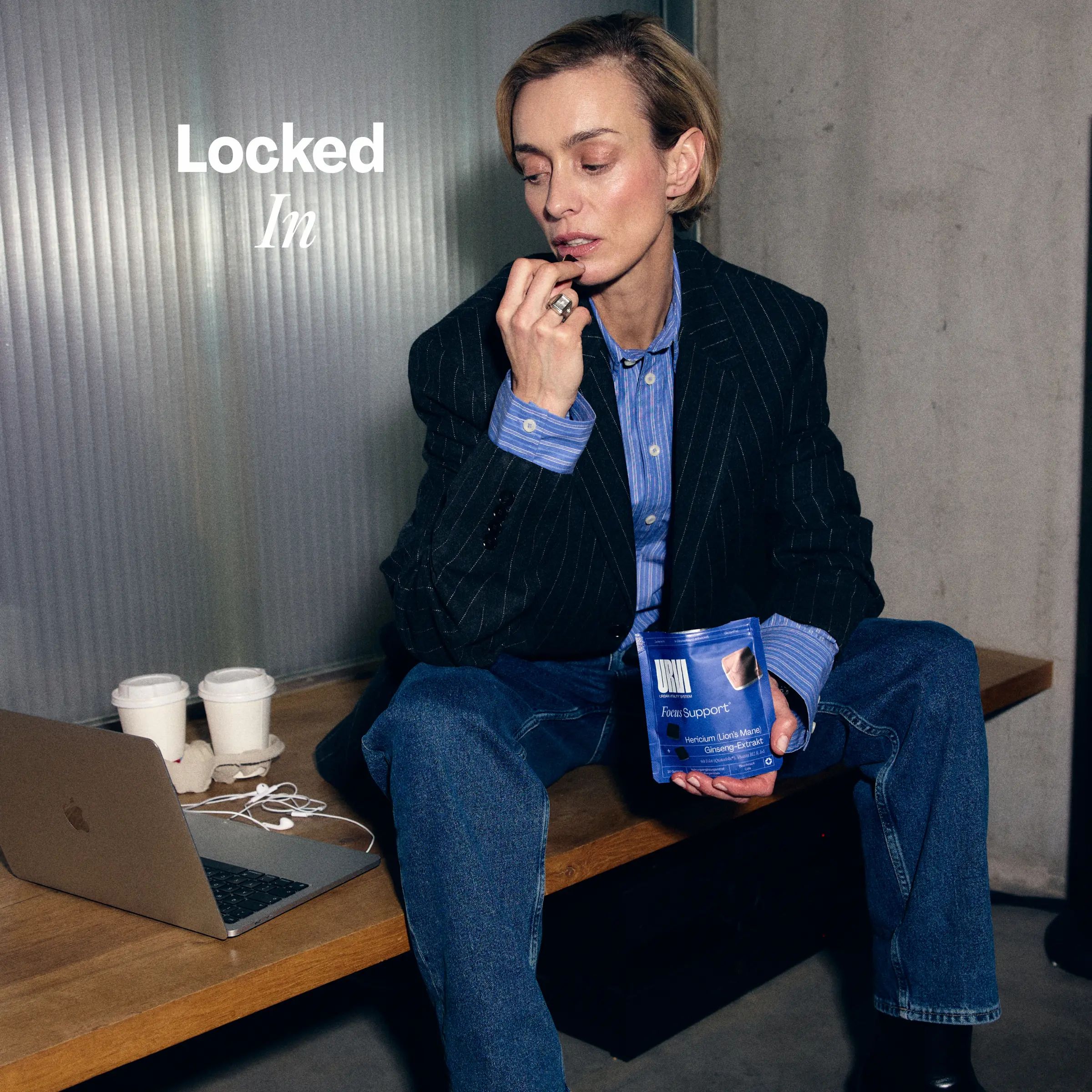 Eine Frau sitzt mit einer Packung Gummibärchen und einer Tasse Kaffee. Ein Laptop ist ebenfalls zu sehen.