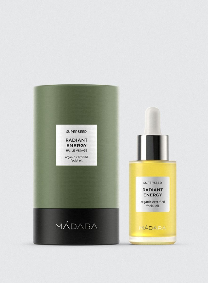 Grüne zylindrische Verpackung und Flasche mit gelbem Öl. Aufschrift: SUPERSEED RADIANT ENERGY, organic certified facial oil, MADARA.