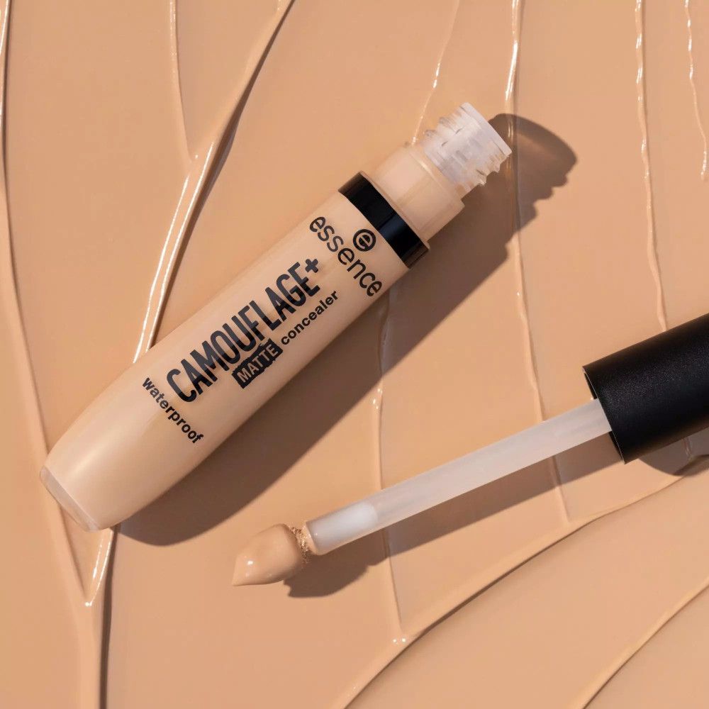 Essence Camouflage+ Matt Concealer, offene Tube mit Applikator. Auf Concealer-Hintergrund.