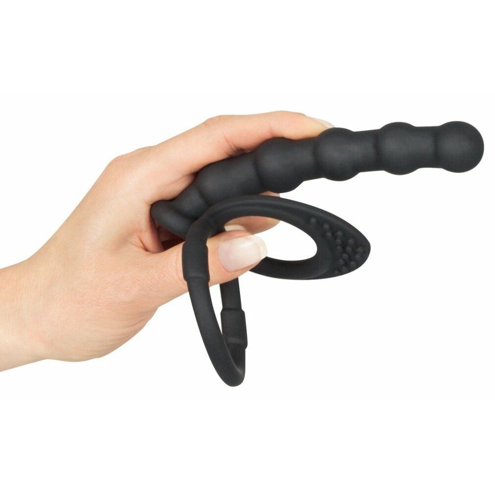 Schwarzer Penis-/Hodenring mit Analdildo. Gehalten von einer Hand. Der Dildo hat eine geriffelte Oberfläche. Der Ring hat eine strukturierte Oberfläche.
