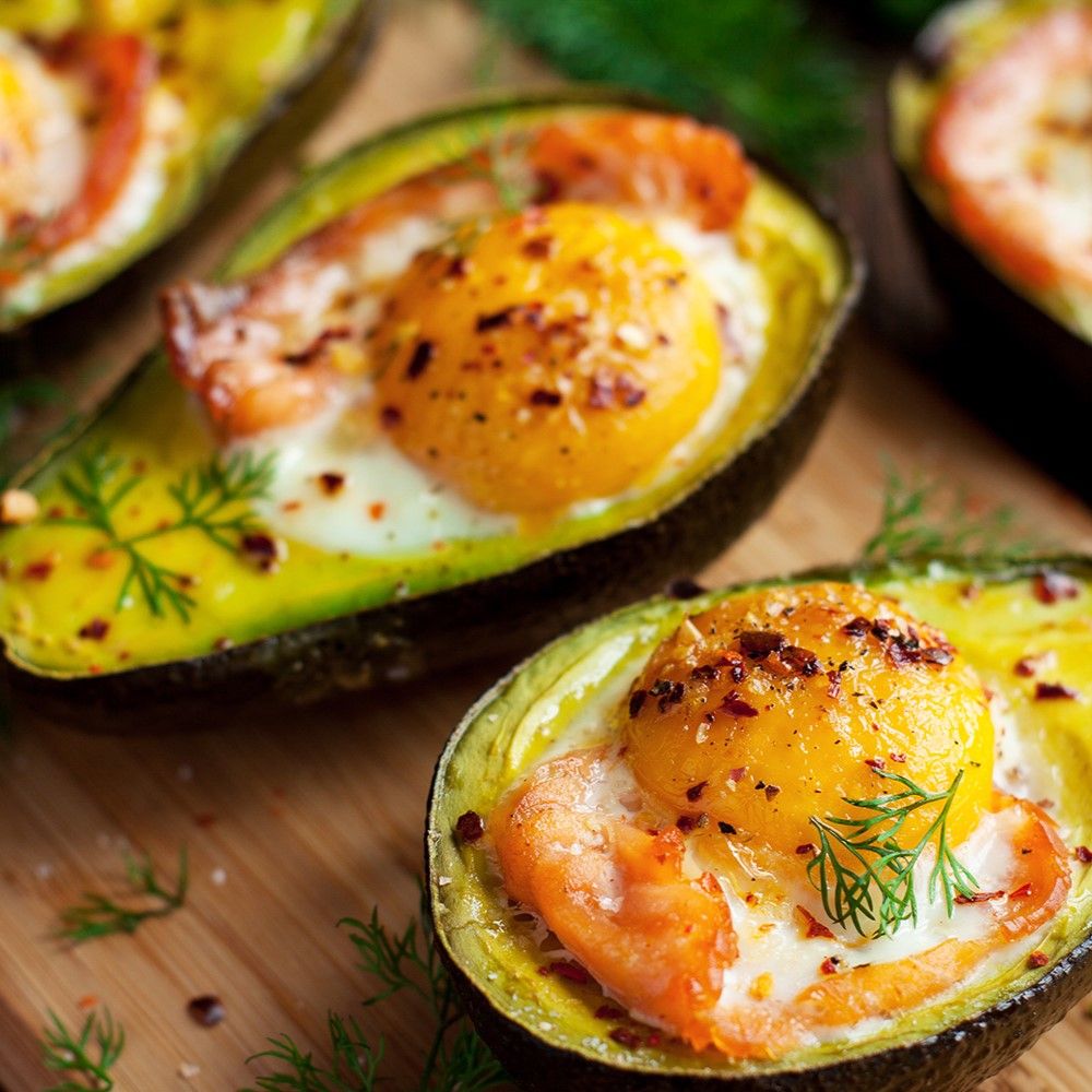 Avocado-Hälften mit Eiern und Garnelen gefüllt. Auf Holzbrett. Mit Kräutern garniert.