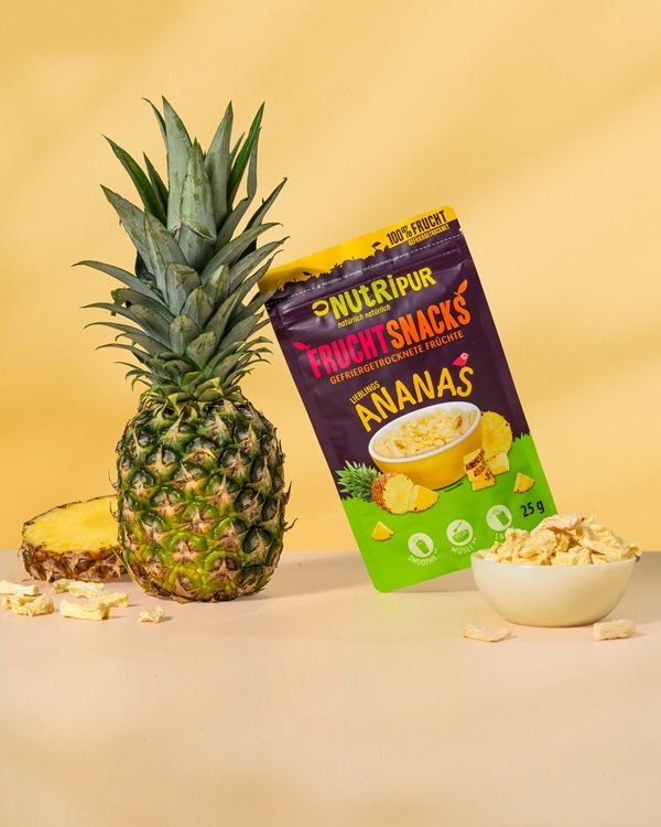Ananas, gefriergetrocknete Ananas-Bits und Verpackung. Aufschrift: "NutriPur Fruchtsnacks Ananas". 25g.