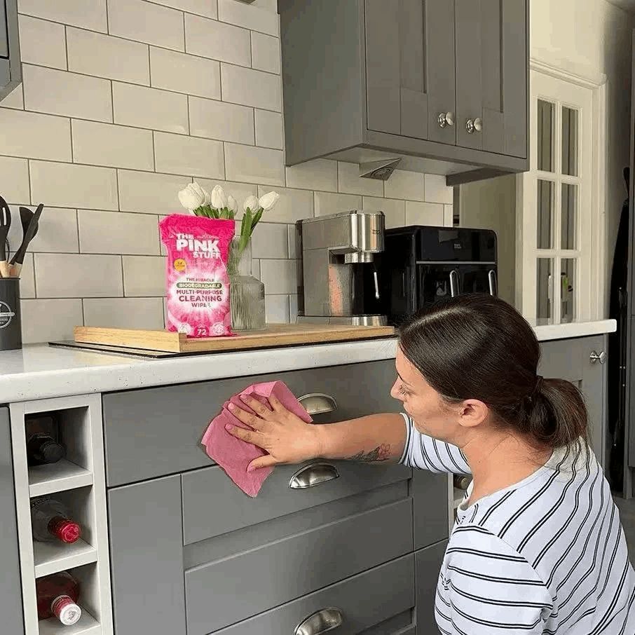 Frau wischt mit einem rosa Tuch eine graue Küchenschublade ab. "THE PINK STUFF" Packung im Hintergrund.