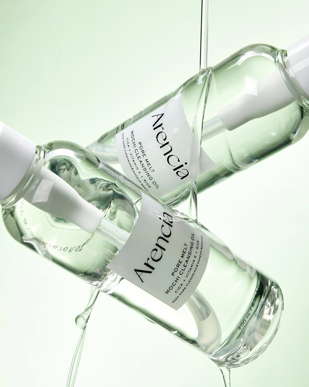 Zwei Flaschen Arencia Pore Melt Mochi Cleansing Oil mit abtropfendem Öl.