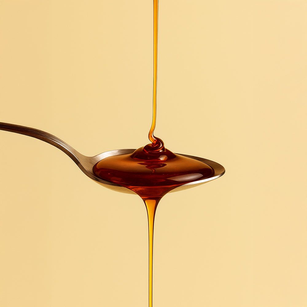 Braune Flüssigkeit fließt von einem Löffel. Hintergrund: hellgelb.