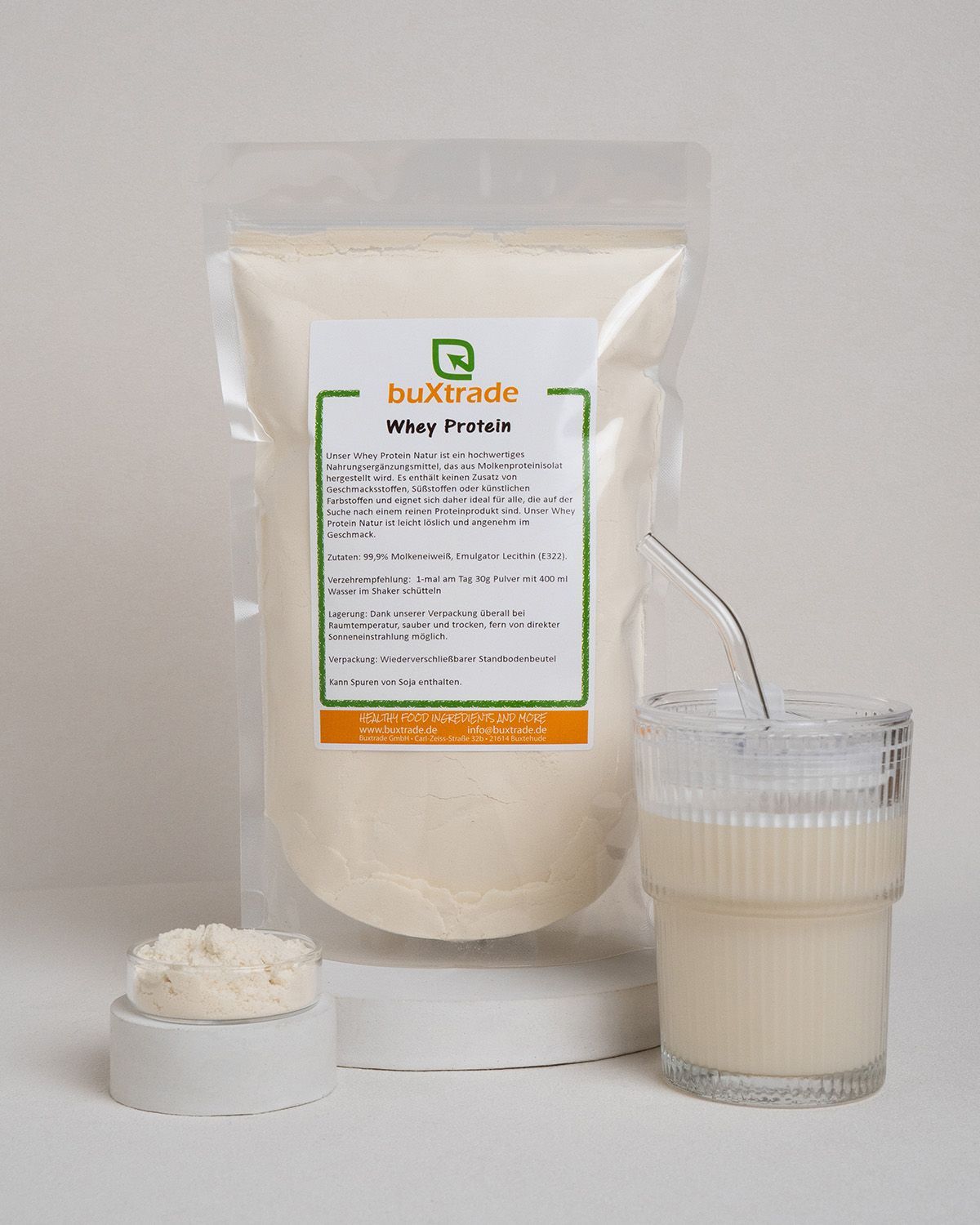 Transparente Beutel, Glas mit Flüssigkeit, Pulver auf Podest. Etikett: buXtrade Whey Protein. Grün-weiß.