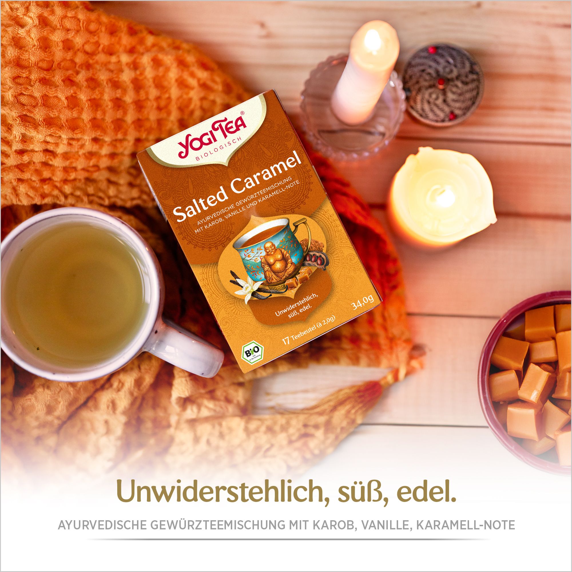 Yogi Tea Salted Caramel Verpackung auf Decke. Daneben Tasse Tee, Kerzen und Karamellstücke. Aufdruck: ayurvedische Gewürzteemischung.