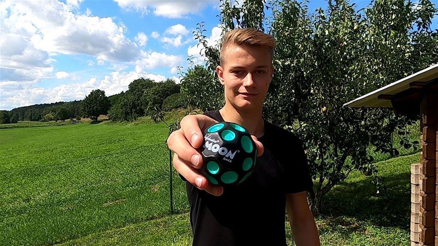 Junge hält Waboba Moon Ball in der Hand. Schwarze Kugel mit grünen Vertiefungen.