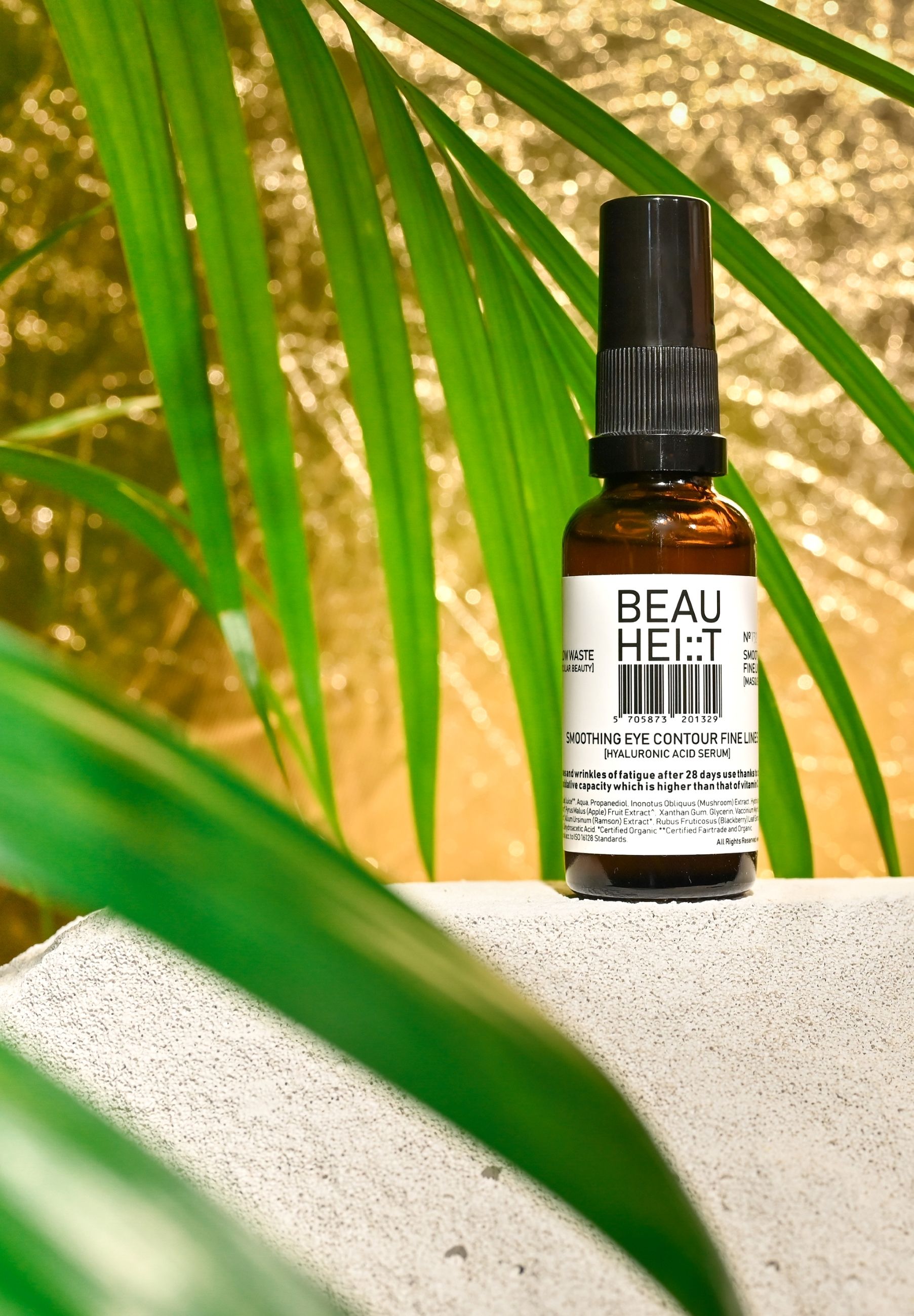 BEAUHEIT Smoothing Eye Contour Fine Lines Gesichtsserum-Flasche vor goldenem Hintergrund und grünen Blättern.