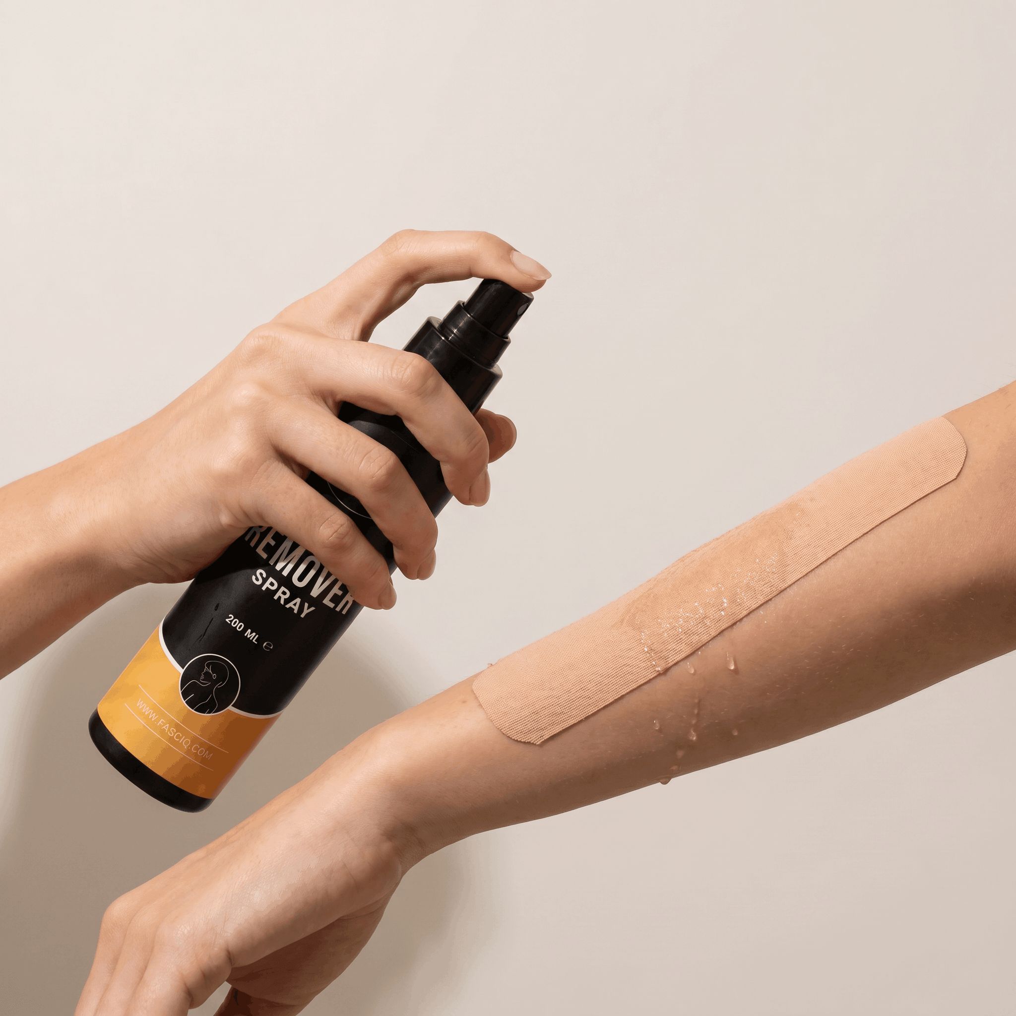 Schwarze Sprühflasche mit der Aufschrift "REMOVER SPRAY" wird auf einen Arm gesprüht, auf dem ein hautfarbener Verband angebracht ist.