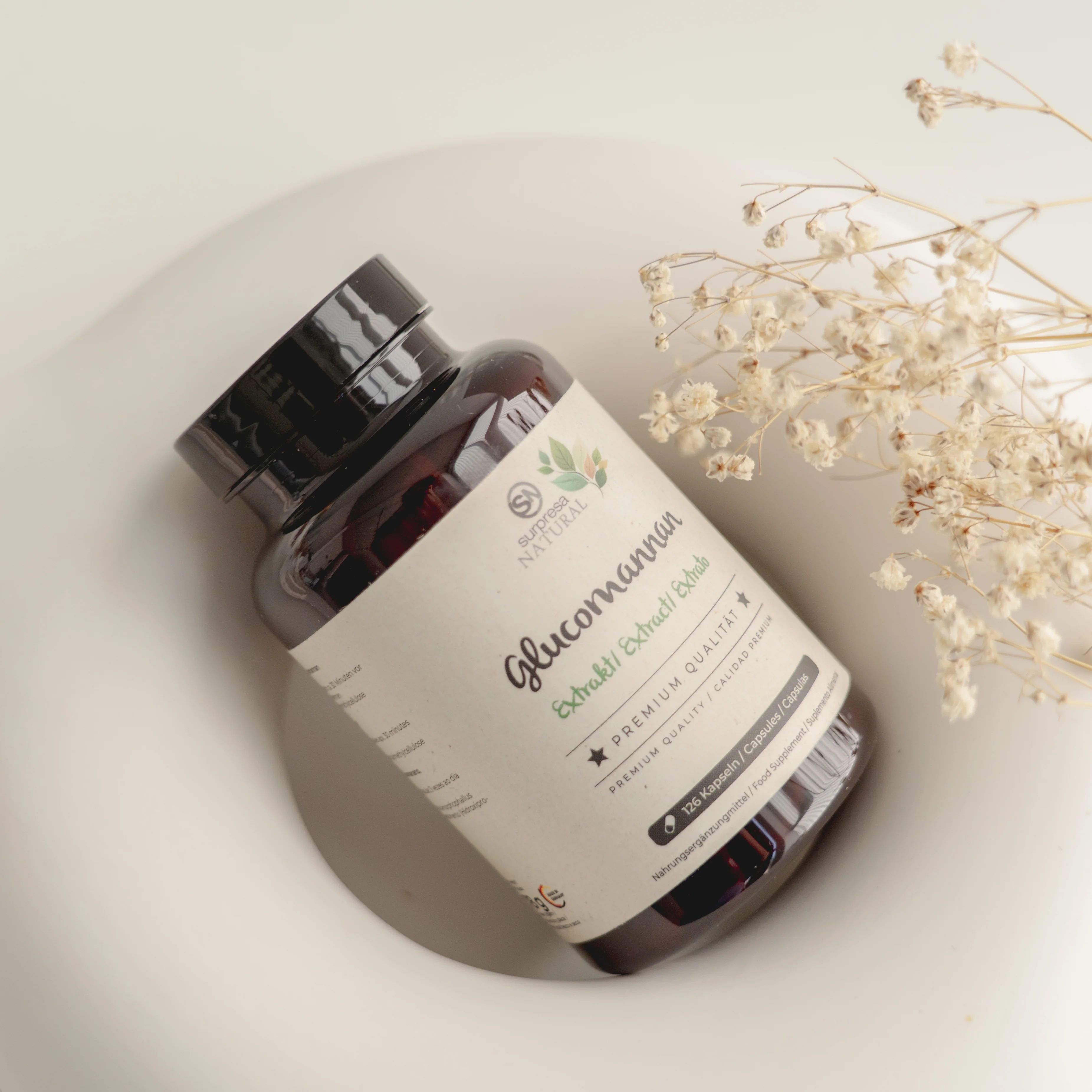 Braune Flasche mit schwarzem Deckel und Etikett. "Surpresa Natural" und "Glucomannan" sind sichtbar. Flasche liegt in einer Schale.