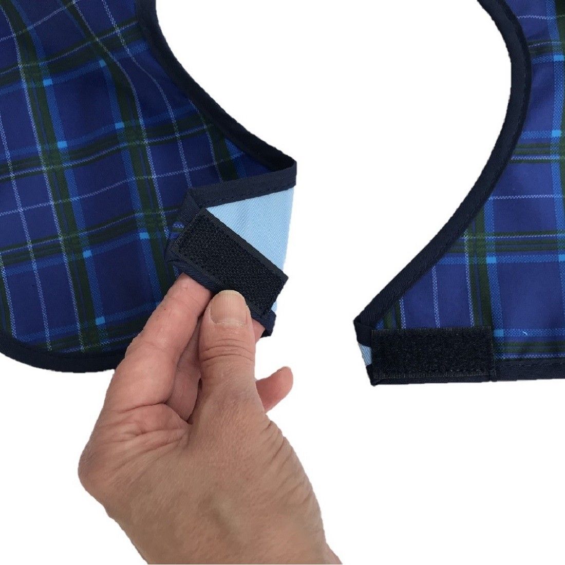Nahaufnahme: Hand öffnet Klettverschluss eines blauen, karierten Lätzchens.