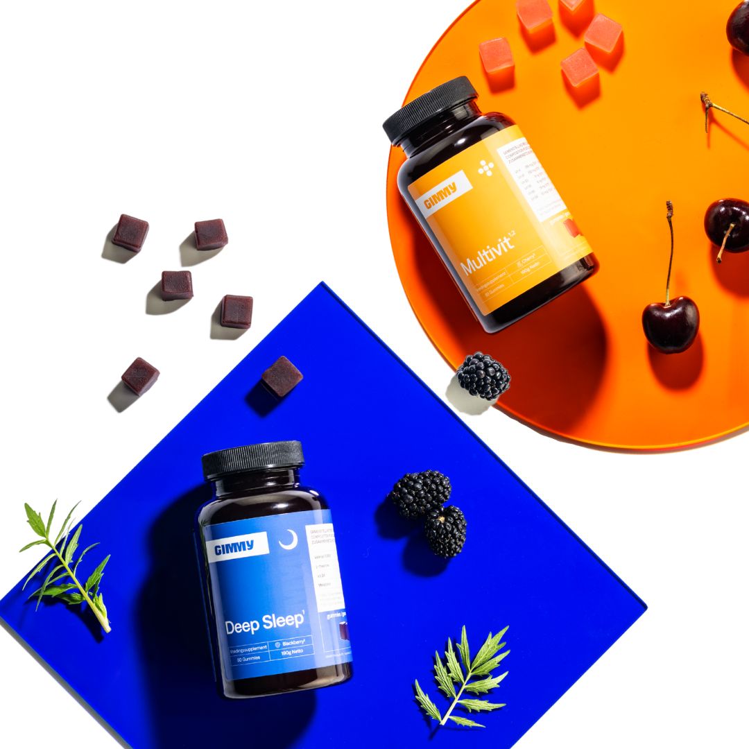Draufsicht. Zwei Flaschen mit schwarzen Deckeln. "Multivit" und "Deep Sleep" Etiketten. Gummibärchen, Brombeeren, Kirschen und Blätter.