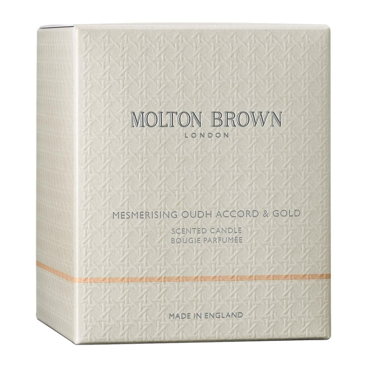 Quadratische Verpackung mit Prägemuster. Aufschrift: Molton Brown London, Mesmerising Oudh Accord & Gold, Scented Candle, Made in England.