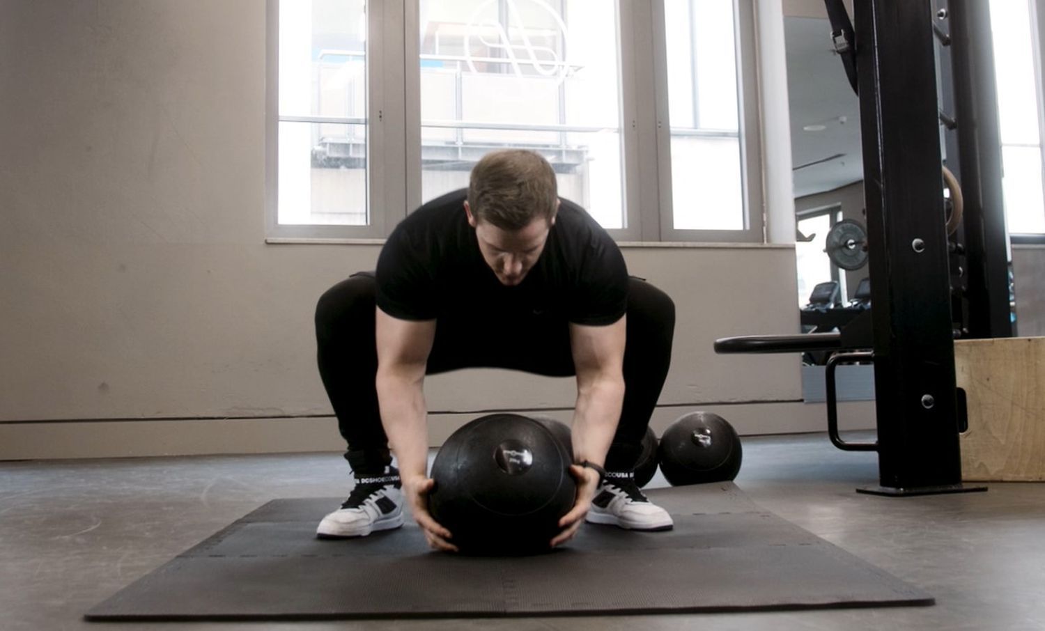 Person in Hocke mit Slamball. Schwarzer Ball, Fitnessstudio-Umgebung.