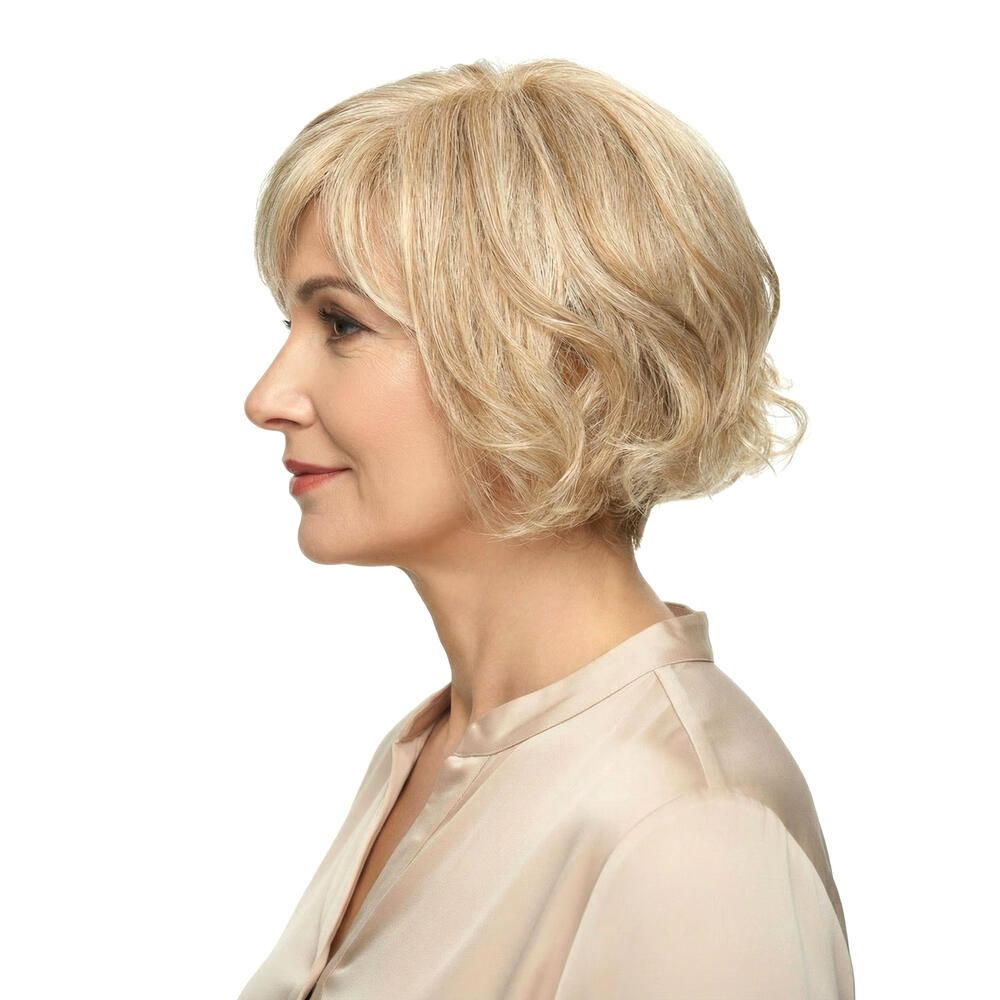 Blonde Perücke mit Pony, welligem Haar. Frau im Profil, beiges Oberteil.