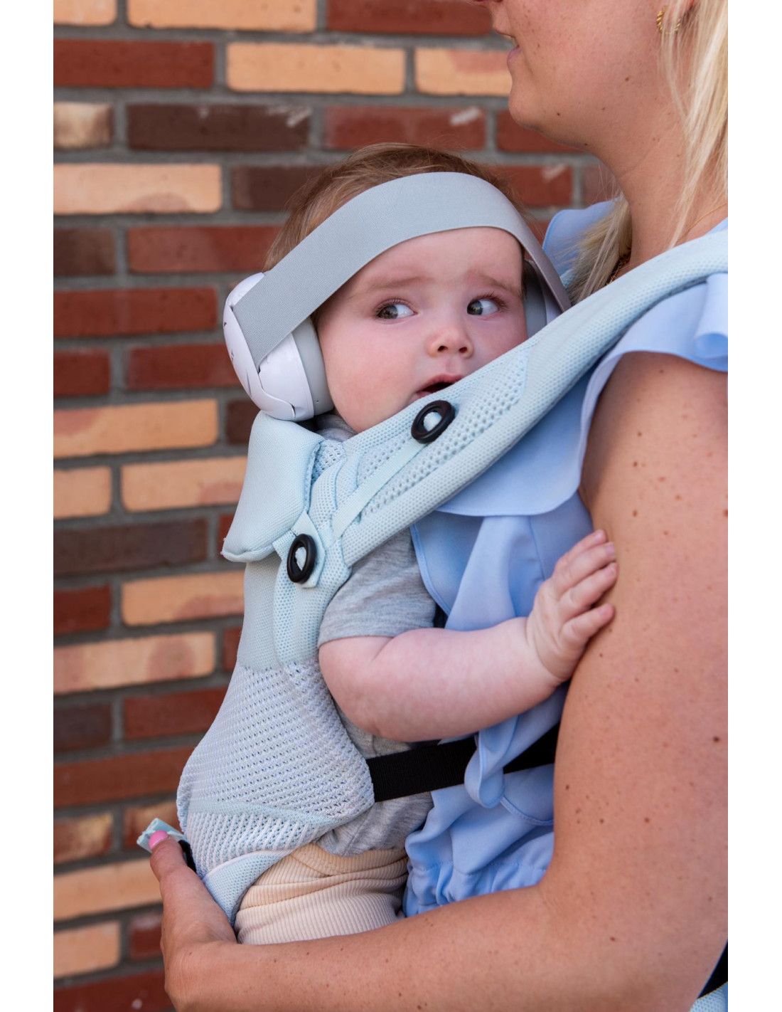 Baby mit weißem Gehörschutz, sitzt in einer Babytrage.