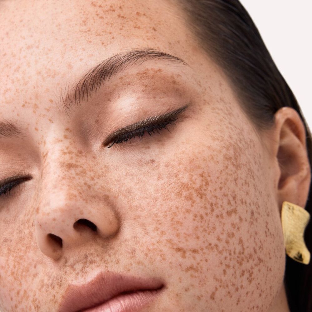 Nahaufnahme eines Gesichts mit Sommersprossen und geschlossenen Augen. Aufgetragenes Augen-Make-up.