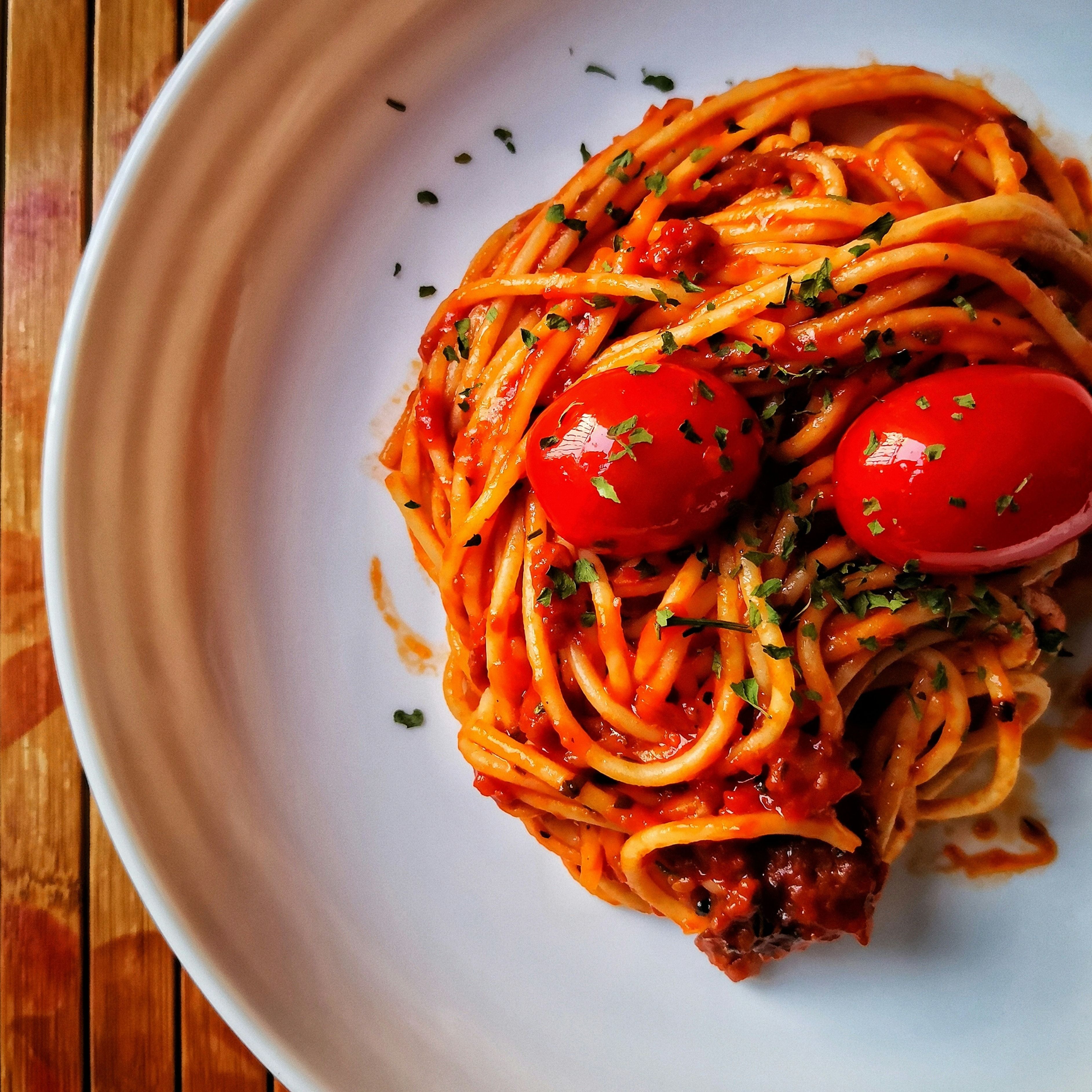 Teller mit Spaghetti Bolognese, garniert mit Cherrytomaten und Kräutern. Draufsicht, auf einem Holzuntergrund.