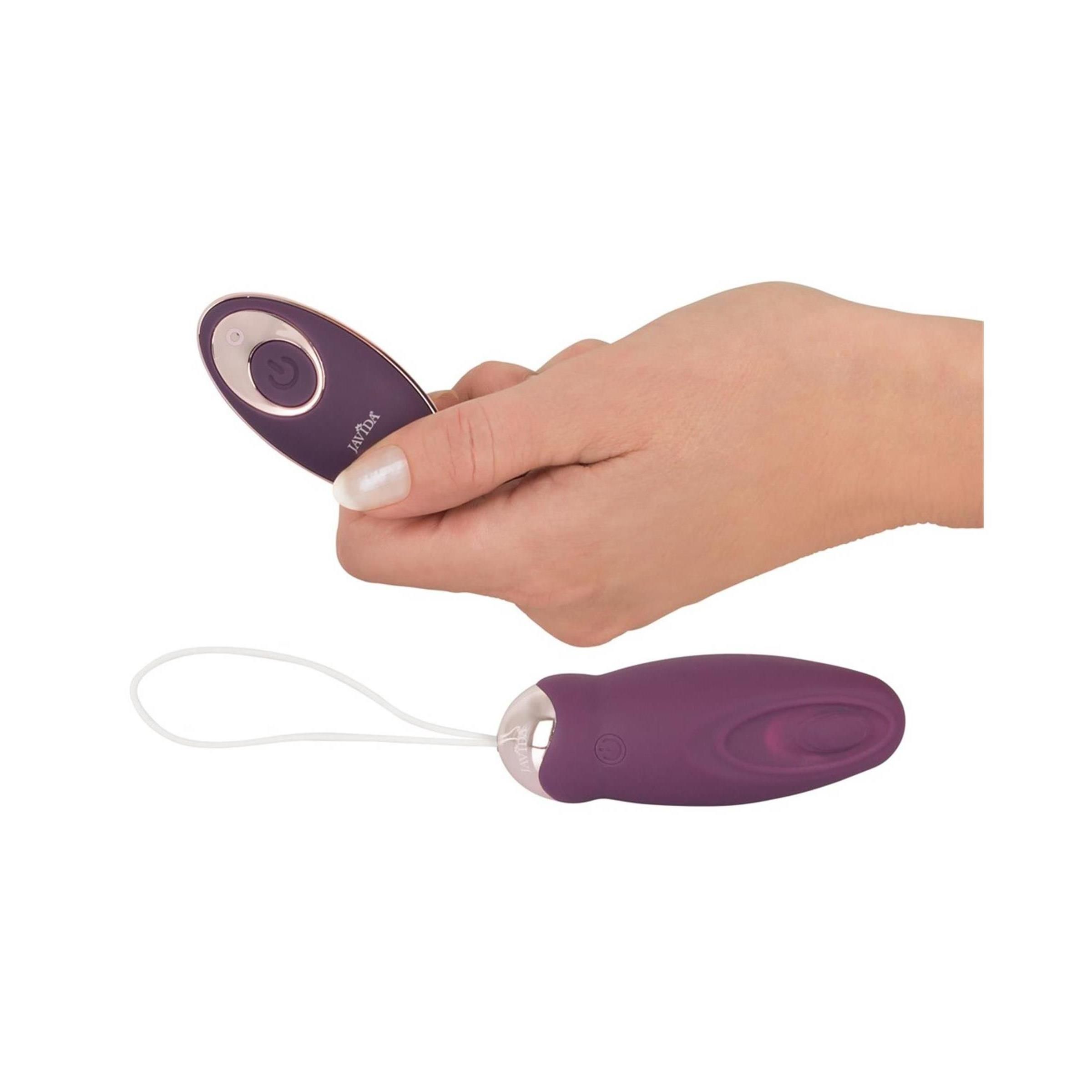 Hand hält Fernbedienung und Vibrationsgerät mit weißer Schlaufe. Auf weißem Hintergrund.