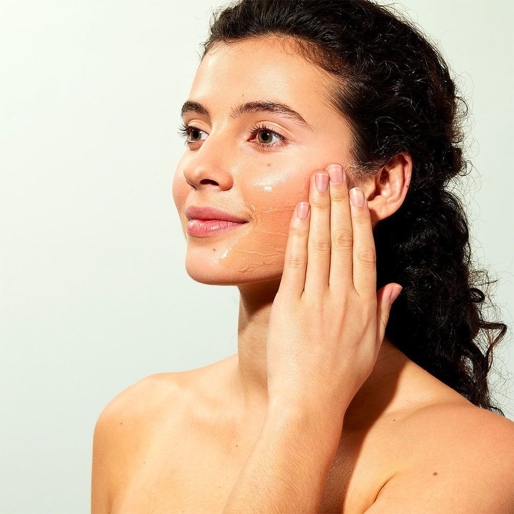 Frau trägt Gesichtsmaske auf. Maske ist transparent. Hintergrund hellblau.
