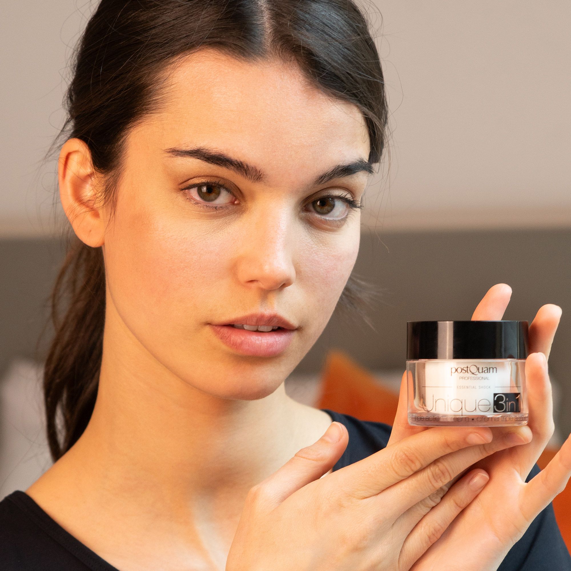 Frau hält Creme-Glas mit schwarzem Deckel. Aufschrift: Postquam Professional, Unique 3in1. Dreifach-Wirkungs-Creme.